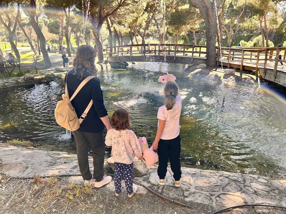 Dorota Anna de espaldas con sus dos hijas frente a la fuente de un parque, las tres cogidas de la mano